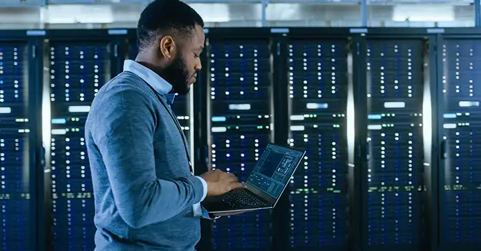 Man stands in front of data center bank with laptop